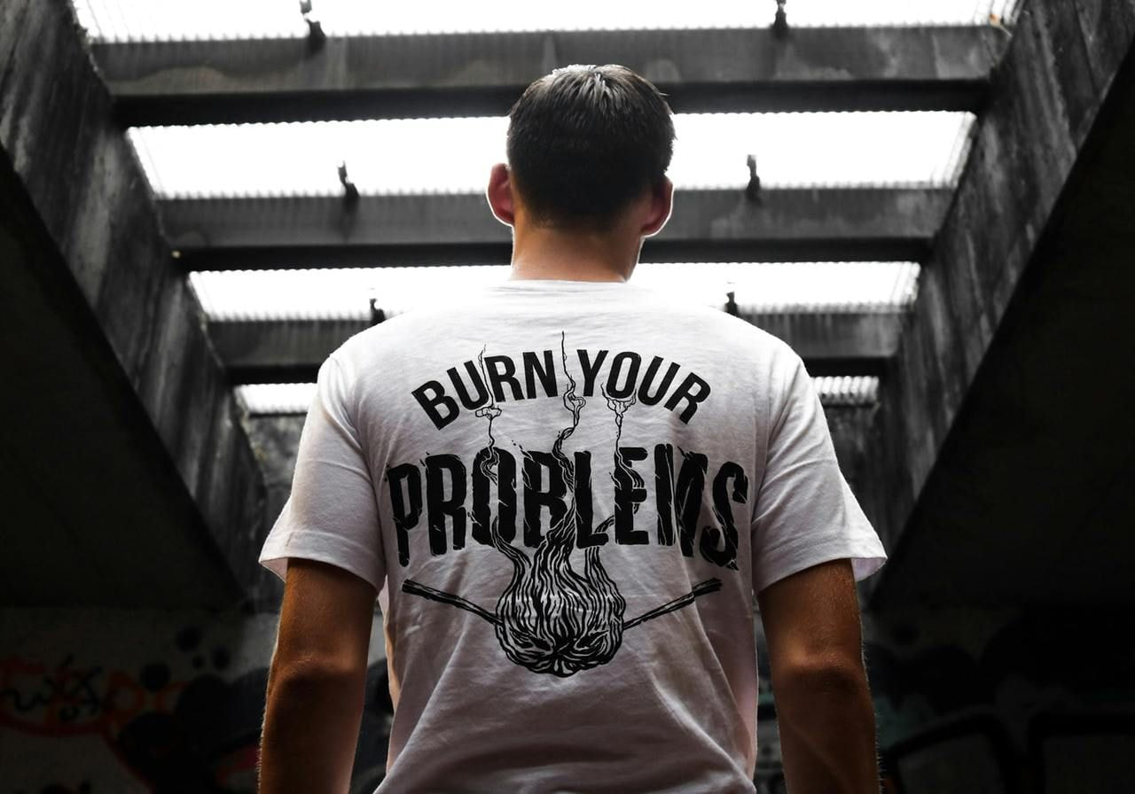 A backshot of a man wearing a white “Burn your problems” t-shirt as an example of a best-selling t-shirt design.